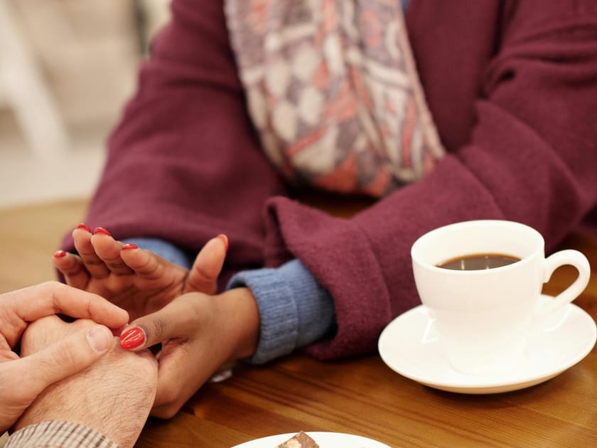 Two people holding hands across a table with coffee cups